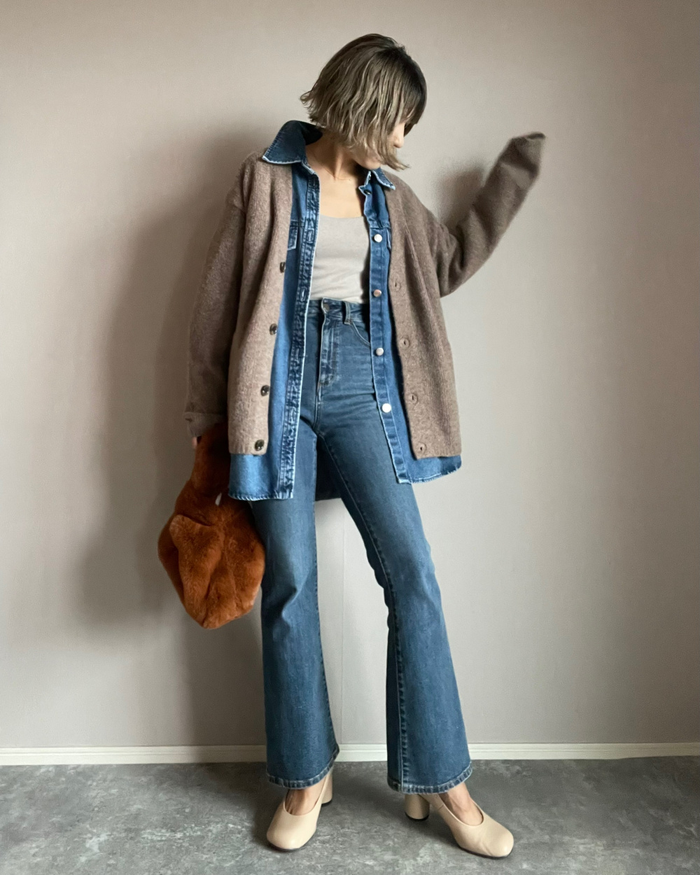 Taupe cardigan layered over an open denim shirt, a pale tank and blue flare jeans