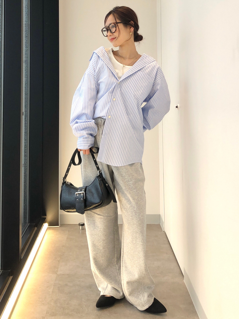 Oversized blue striped shirt partly tucked into gray wide-leg sweatpants, worn with black pointed flats