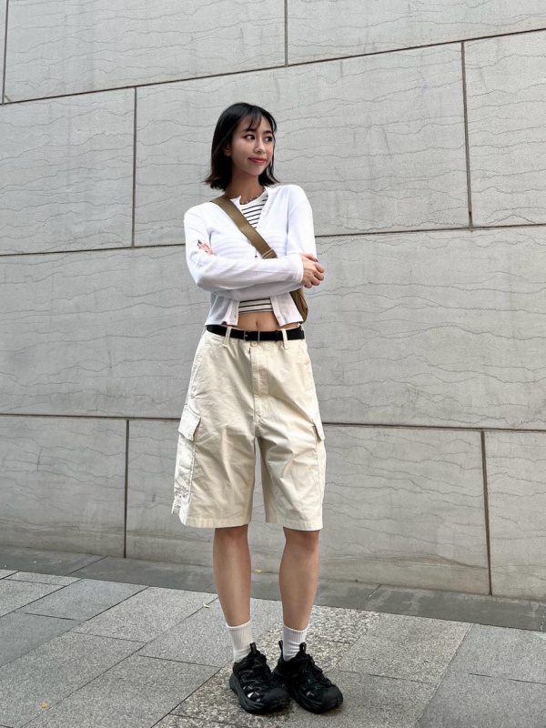 Woman wearing cream knee-length cargo shorts with a cropped cardigan, crossbody bag and chunky sneakers